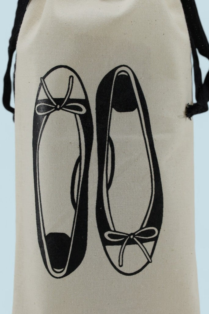 Sac à chaussures de voyage Moonlac étroit en coton écru, sérigraphié de ballerines avec nœuds, cordons noirs, posé debout sur fond bleu