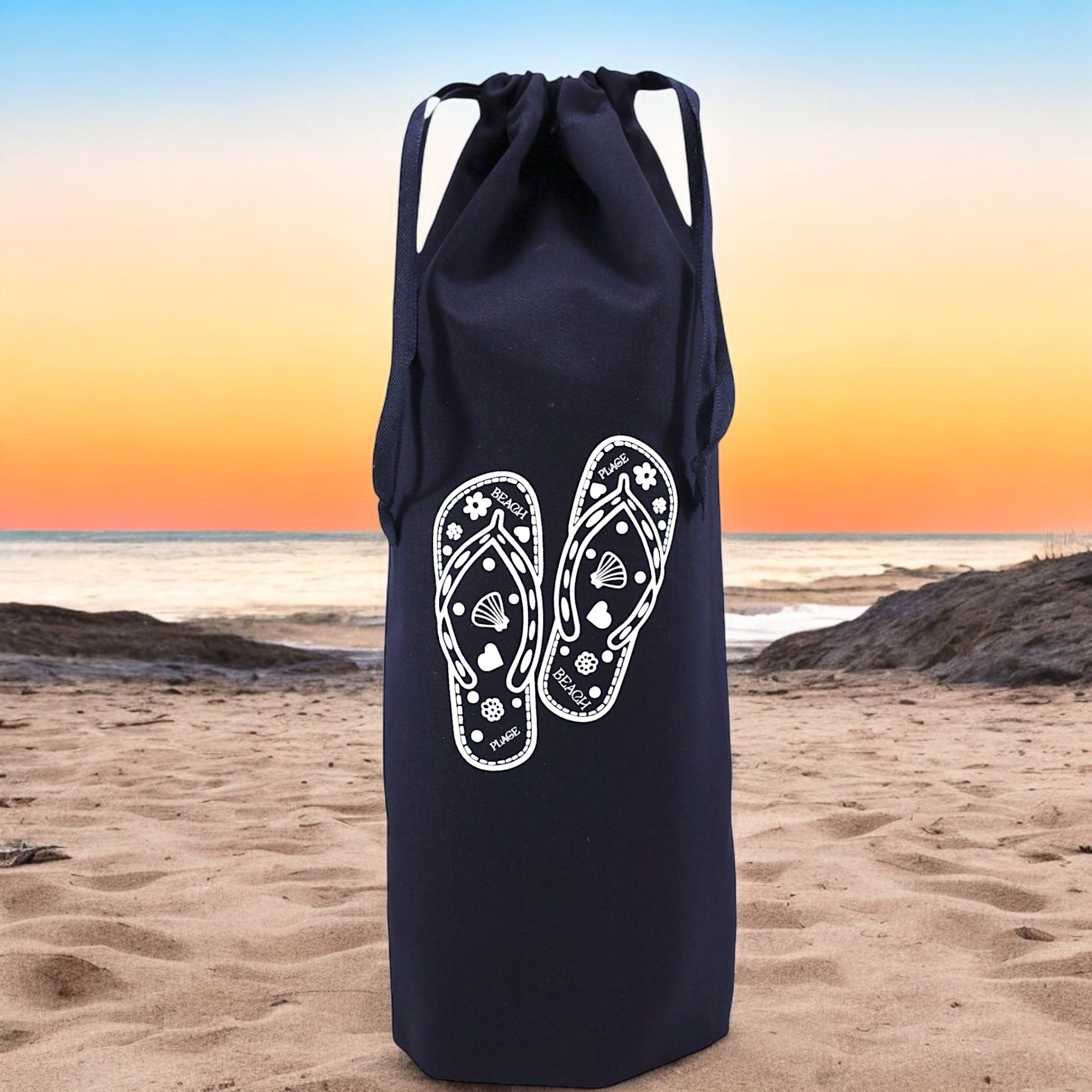 Pochon bleu marine Moonlac avec dessin de tongs, posé face à un coucher de soleil – accessoire estival idéal pour une valise pleine de soleil.