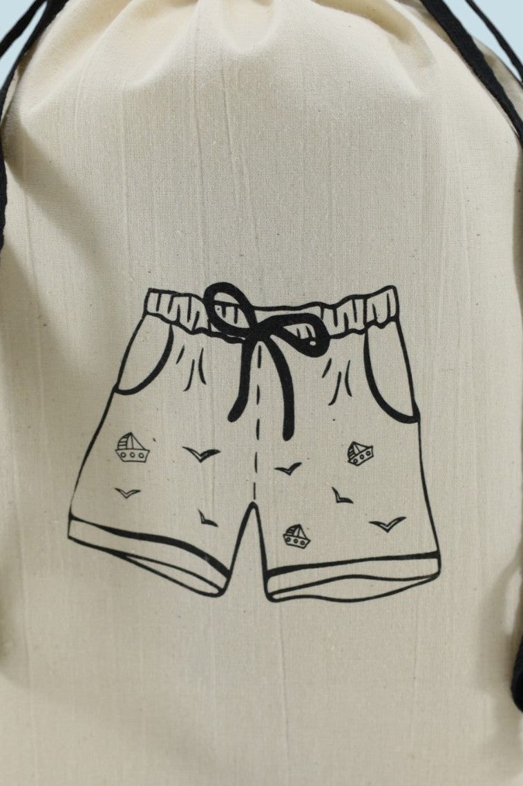 Pochon Moonlac en coton écru, sérigraphié d’un short de bain noir, posé debout avec cordons noirs contrastants