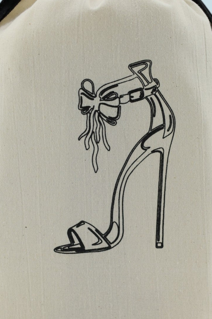 Sac Moonlac en coton écru avec sérigraphie noire d’un escarpin à talon haut orné d’un nœud, cordons noirs. Organisateur de valise